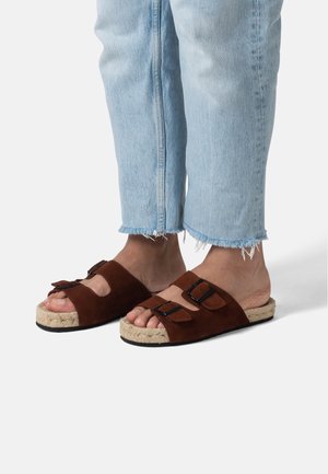 Brune ruskindssandaler med to justerbare remme, en jute-indhyllet sål og en sort gummisål. Båret med lys blå slidte jeans.