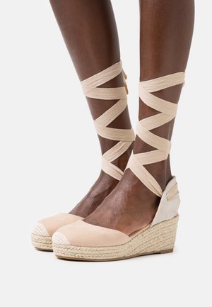 Espadrilles compensées en daim beige avec semelles en jute tissé. Lanières crème ajustables qui s'enroulent autour des chevilles. Bout fermé avec détail de bout contrastant.