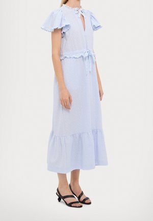 Femme portant une robe midi bleu clair à manches volantées, encolure goutte d'eau, ceinture à la taille, et des talons noirs à lanières avec talons arrondis.