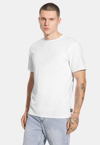 Biała, krótki rękaw t-shirt z bawełny, z okrągłym dekoltem i luźnym krojem, noszony z jasnoniebieskimi dżinsami.