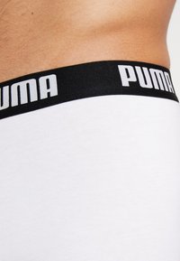 Valged puuvillased bokserpüksid musta elastse vööga, millel on marki "PUMA" esitatud paksude valgete tähtedega, sile tekstuur.