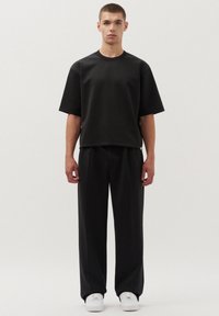 Zwarte top met korte mouwen en wijdvallende broek van gladde stof, gecombineerd met witte sneakers. Eenvoudig ontwerp met een ongestructureerde pasvorm.