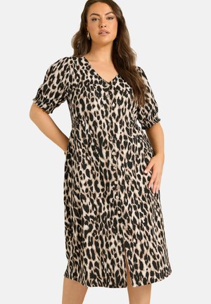 Kvinde iført en knælængde kjole med knapper foran i et brunt og sort leopardmønster og korte pufærmer.