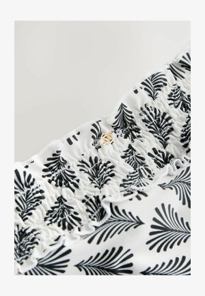 Mustavalkoinen kukkakuosisella kankaalla, jossa on koottu rakenne ja kultainen korostusnappi yläreunassa. Pehmeä, kevyttä materiaalia.