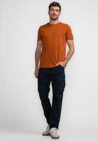 Tangerine kleurige katoenen t-shirt met een ronde halslijn en een klein logo op de borst, gecombineerd met marineblauwe cargo-broeken met meerdere zakken en een ontspannen pasvorm.