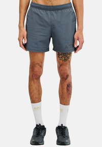 Graue Sportshorts mit einem elastischen Bund, Logodetail auf der linken Seite, getragen mit schwarzen Sneakers und weißen Socken mit Text.