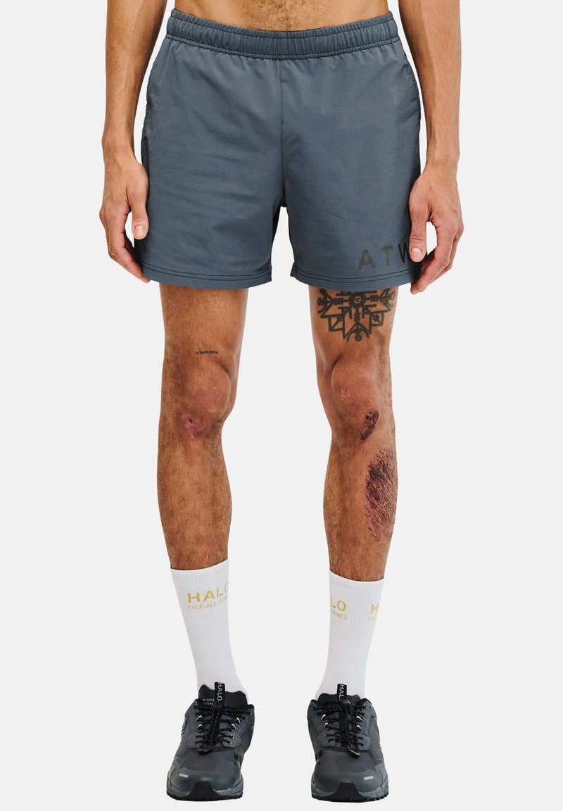 Graue Sportshorts mit einem elastischen Bund, Logodetail auf der linken Seite, getragen mit schwarzen Sneakers und weißen Socken mit Text.