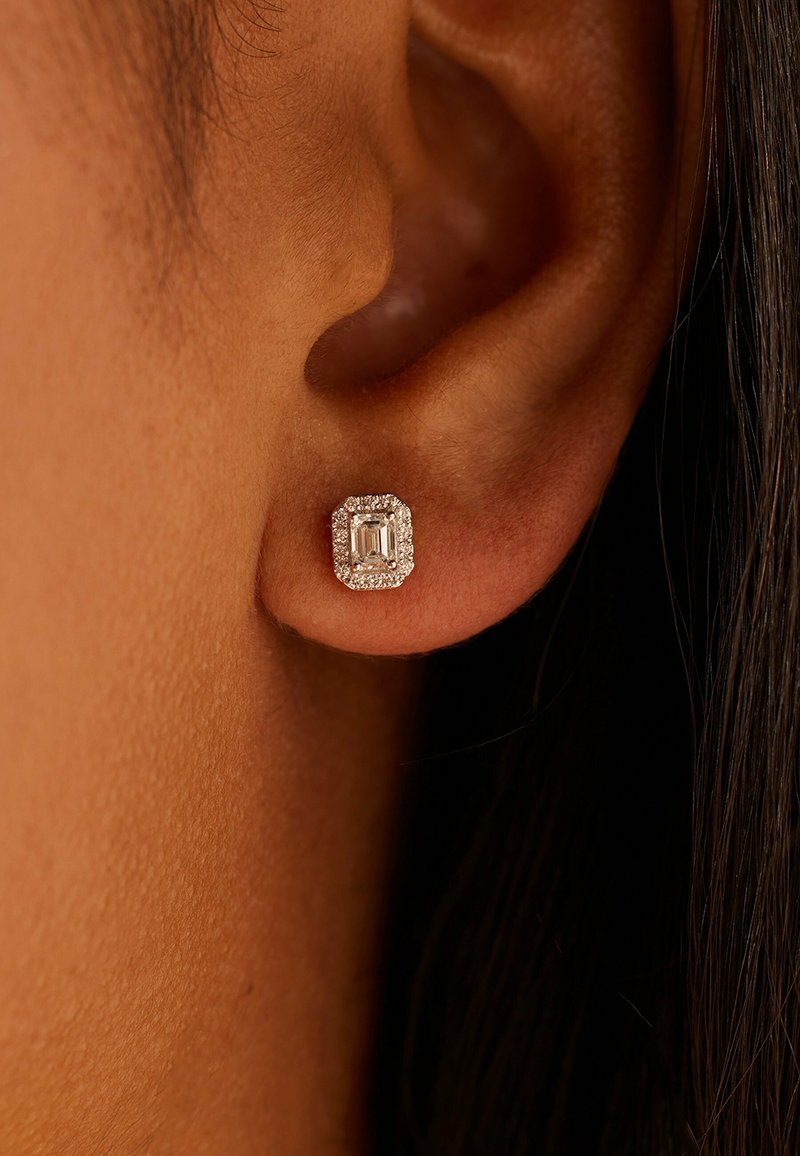 Quadratischer Ohrstecker mit einem klaren, smaragdgeschliffenen mittleren Stein, umgeben von einem Kranz kleiner weißer Steine, gefasst in glänzendem Metall.