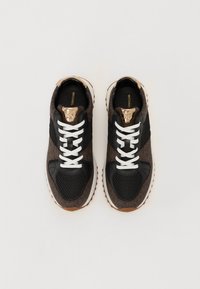 Baskets de sport noires et marron avec des textures en maillage et lisses, lacets blancs, accents dorés sur la languette et un détail latéral à motifs.