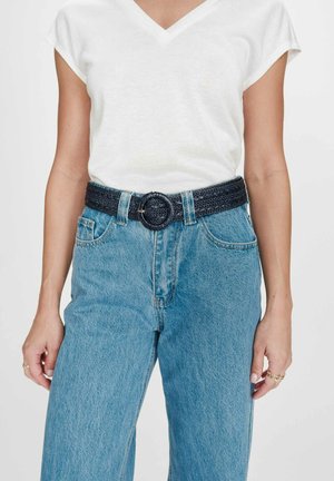 Femme portant un t-shirt blanc à manches courtes et col en V, rentré dans un jean taille haute bleu avec une ceinture tissée noire à boucle ronde.