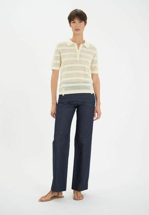 Polo beige à rayures avec des manches courtes et un col, associé à un pantalon large noir et des sandales beiges. Le tissu semble léger et texturé.