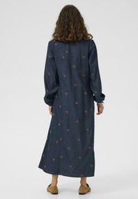 Maxikleid aus Denim mit langen Ärmeln, floralem Stickereien in Braun. Gerader Schnitt mit Rückenpasse und seitlichen Schlitzen für uneingeschränkte Bewegungsfreiheit.