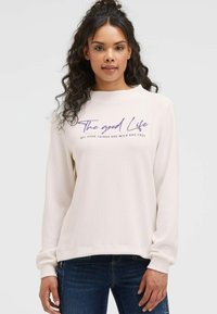 Hellbeige Sweatshirt aus strukturiertem Stoff, mit rundem Ausschnitt, langen Ärmeln und lila Text: "Das gute Leben" und "ALLE GUTEN DINGE SIND WILD UND FREI."
