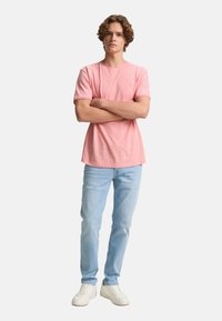 Camiseta rosa claro de manga corta con cuello redondo, combinada con jeans de mezclilla azul claro y zapatillas blancas. Diseño simple, sin patrones visibles.