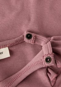 Roze katoenen stof met een gladde textuur, voorzien van een drukknoopsluiting op de schouder en zichtbare stikdetails. Label bevestigd.
