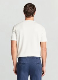 Kurzärmliges, weißes, geripptes Shirt kombiniert mit marineblauen Hosen mit glatter Textur und hinten mit Knopftaschen.