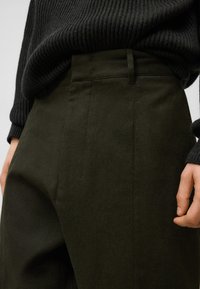 Donkergroene broek gemaakt van gestructureerde stof, met een hoge taille, zijzakken en een getailleerde pasvorm, gecombineerd met een zwart geribbeld sweater.