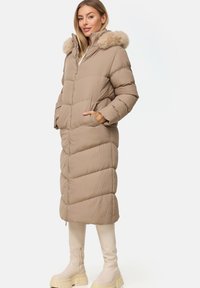 Beige gepolsterter Mantel mit einer mit Fell besetzten Kapuze, ausgestattet mit einem Reißverschluss vorne, seitlichen Taschen und einem langen, geraden Design. Dicke, strukturierte Stoff.