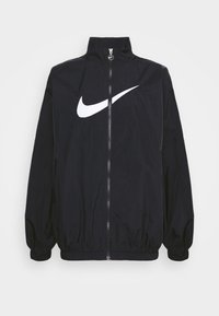 Črn Nike vetrovka z visokim ovratnikom, polnim zadrgo, elastičnimi manšeti in velikim belim logotipom swoosh spredaj. Lahka, gladka tekstura.
