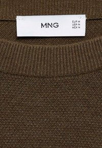 Brauner Strickpullover aus Material mit einem gerippten Rundhalsausschnitt. Das Etikett zeigt die Marke "MNG" sowie Größeninformationen in europäischen, US-amerikanischen und mexikanischen Formaten an.