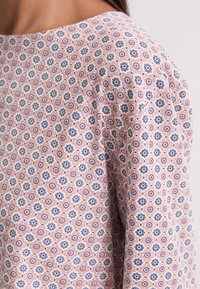 Gros plan sur une chemise en tissu rose avec un motif floral répétitif bleu et blanc, portée sur l'épaule et le haut du bras d'une personne.