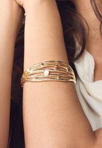 Gold-tone multi-strand bracelet with varying gemstones, featuring circular accents and a smooth, textured surface.