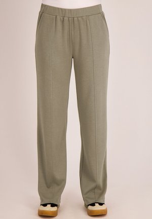 Loszittende olijfgroene broek met elastische tailleband en voornaaddetails, gedragen met wit-zwarte sneakers.