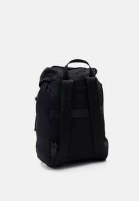 Mochila negra con diseño enrollable, fabricada en nylon duradero. Cuenta con correas de hombro acolchadas, bolsillo lateral y una textura suave y mate.