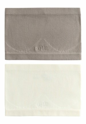 Frau mit lockigem Haar, die ein taupefarbenes, geripptes Bandeau und weiße Unterwäsche mit dem "self."-Logo trägt, richtet ein hellblau gestreiftes Hemd von den Schultern.