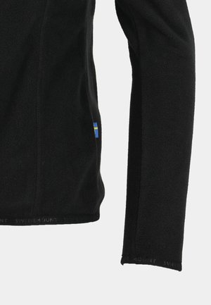 Schwarze Fleecejacke mit strukturierter Oberfläche und einem schwedischen Flaggen-Detail an der Seite. Verfügt über lange Ärmel und einen geraden Saum.