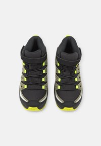 Buty sportowe za kostkę z czarną tekstylną cholewką, zielonymi akcentami i wzorzystym designem. Wyposażone w pasek na rzep oraz zaokrągloną gumową podeszwę.