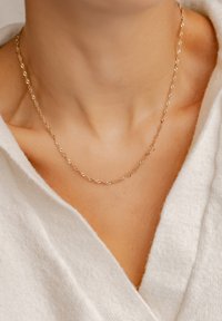 Collana a catena dorata attorcigliata posata su un collo nudo, con un design delicato e maglie lisce e lucide su un tessuto chiaro.