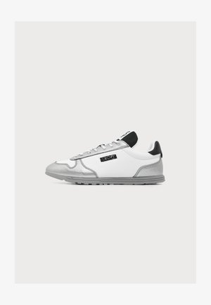 Valge toss hõbedaste detailidega, halli tallaga, musta kannarihmaga ja DKNY logoga küljel, esitatud tavalise valge taustal.