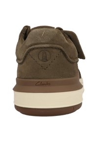 Bruine suede schoen met een gewatteerde kraag en een witte tussenzool. Clarks-logo is in de hiel geperst. Voorzien van een klittenbandsluiting.