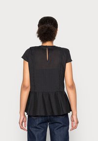 Top peplum negro con un panel trasero texturizado con rayas verticales, mangas cortas y un detalle de abertura en el escote.
