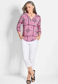 Roze blouse met patroon, 3/4 mouwen, V-hals en een vloeiende ontwerp; gecombineerd met witte cropped broeken en zwarte sandalen.