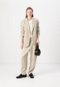 béžový oversize blazer, textúrovaný biely pletený top, voľné béžové nohavice, čierne kožené topánky a čierna kabelka s rukoväťou.