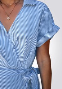 Vestido envolvente de rayas azules y blancas con mangas cortas dobladas, que presenta un detalle de cintura anudada y un diseño de escote en V. Textura de tela suave.