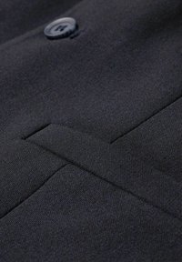 Black fabric with a subtle texture, featuring a button and a slanted pocket. The design is simple and tailored.