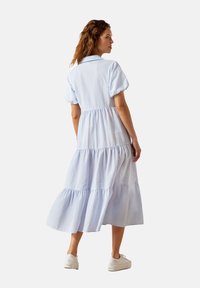 Gestreiftes Kleid in Blau und Weiß mit schichteten, kurzen Puffärmeln, Kragen und gerafftem Taillenbereich. Kombiniert mit weißen Sneakern.