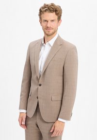 Hellbrauner Blazer mit strukturiertem Finish, einreihiger Schnitt, Reverskragen und zwei aufgesetzten Taschen. Darunter ein weißes Hemd mit Knopfleiste.