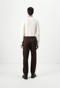 Kabelgebreide crèmekleurige trui met een ronde hals, gecombineerd met donkerbruine rechte broek. De outfit heeft een gestructureerd breisel en aansluitende manchetten.