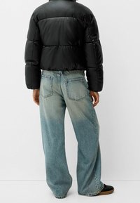 Svart vadderad jacka med kort design, parat med ljusblå jeans med en blekt textur och vid benmodell.