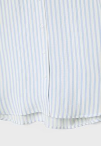 Hellblau-weiß gestreifter Stoff eines Hemdes mit sichtbaren weißen Knöpfen und einem leicht geschwungenen Saum am unteren Rand.