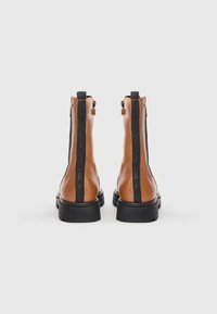 Botas de tobillo de cuero marrón con paneles laterales texturizados en negro, suela gruesa negra y cierre de cremallera con una lengüeta en la parte trasera.