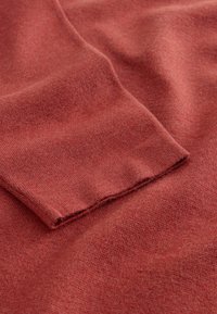 Tissu en tricot rouge à la texture douce, présentant un pli et un ourlet à bords francs. Couleur lisse et uniforme avec une apparence décontractée.