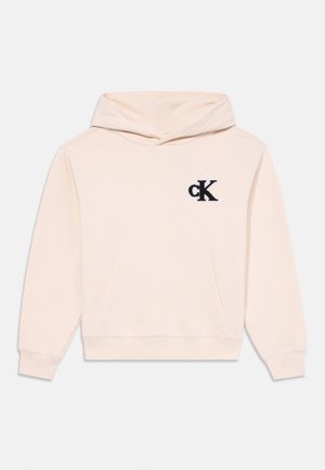 Svetlo béžová mikina vyrobená z mäkkej látky, s prednou kapsou a vyšitým tmavomodrým logom "cK" na hrudi. Nastaviteľná kapucňa.