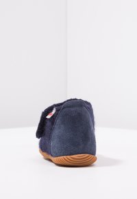 Granatowe wełniane kapcie o teksturowanym wykończeniu, wyposażone w solidną gumową podeszwę i regulowany pasek zapewniający pewne dopasowanie.