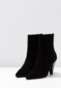 Czarne zamszowe botki za kostkę z ostrym noskiem, zwężającym się obcasem i gładką teksturą. Charakteryzują się czystą sylwetką i minimalnymi detalami.