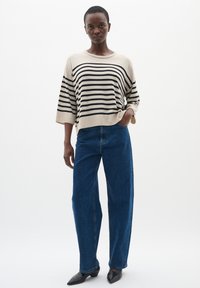 Maglione a strisce beige e nere con maniche ampie, abbinato a jeans blu a gamba dritta con vita alta e scarpe con tacco a punta nere.